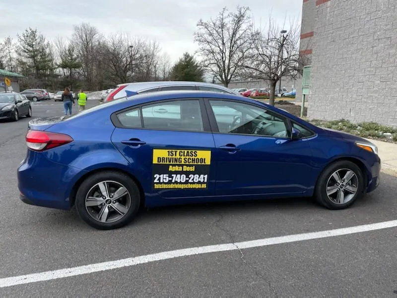Blue driving-school sedan with door signage in a parking lot