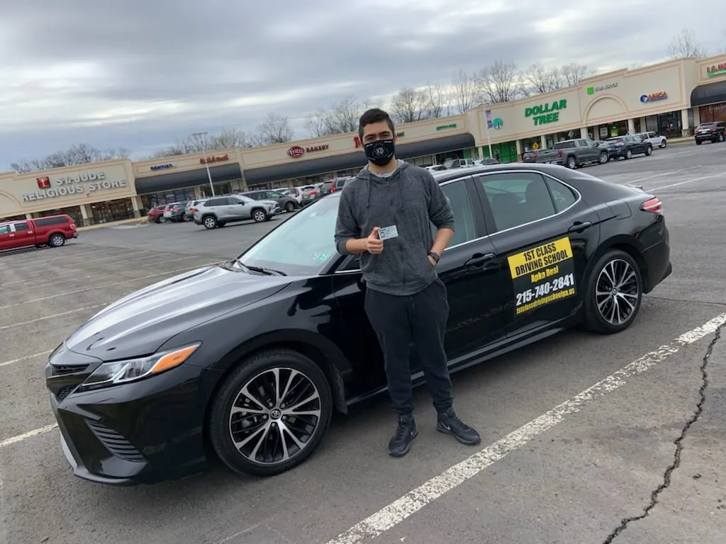 Student beside the black dual-control training car in a parking lot